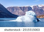 A blue iseberg in the waters of Dickson fjord, Northeast Greenland National Park. The Hisinger glacier and snow covered mountains can be seen behind.