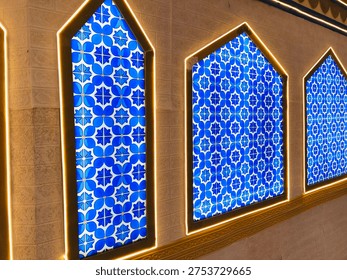 Blue Islamic geometric pattern displayed on mosque wall panels with illuminated arch frames. Traditional Islamic art and architectural decoration. 