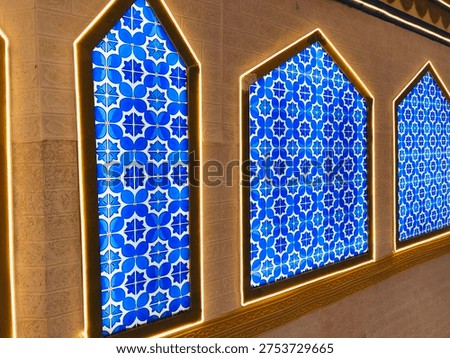 Blue Islamic geometric pattern displayed on mosque wall panels with illuminated arch frames. Traditional Islamic art and architectural decoration. 