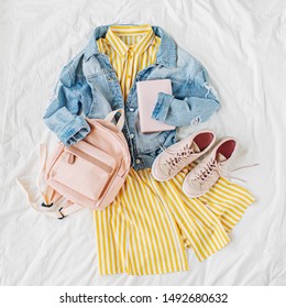 Blue Jean Jacket And Yellow Dress  With Backpack, Book And Sneakers On White. Women's Stylish Autumn Or Spring Outfit. Trendy Clothes For College. Back To School Concept.  Flat Lay, Top View.