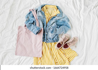 Blue Jean Jacket And Yellow Dress  With Eco Bag And Sneakers On White Bed. Women's Stylish Autumn Or Spring Outfit. Trendy Clothes With White Eco Bag Mockup. Fashion Concept.  Flat Lay, Top View.