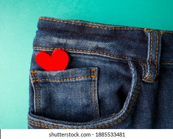 Blue jeans and one red heart lies in the front pocket of jeans on a green background - Powered by Shutterstock