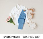 Blue jeans, white shirt, heeled sandals, bag with chain strap, jewelry, bouquet of pink tulips flowers on beige background. Women