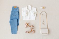 Blue jeans, white shirt, pink heeled sandals,  small cross body bag with chain strap, jewelry, accessories on beige background. Women's stylish spring summer outfit. Trendy clothes. Flat lay, top view, a Beauty & Fashion Photo by Nesolenaya Alexandra
