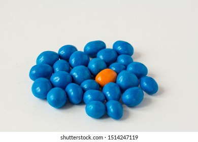 A Lot Of Blue Jelly Beans And One Orange Jelly Beans On A White Background. Concept Be Original. To Be An Individual