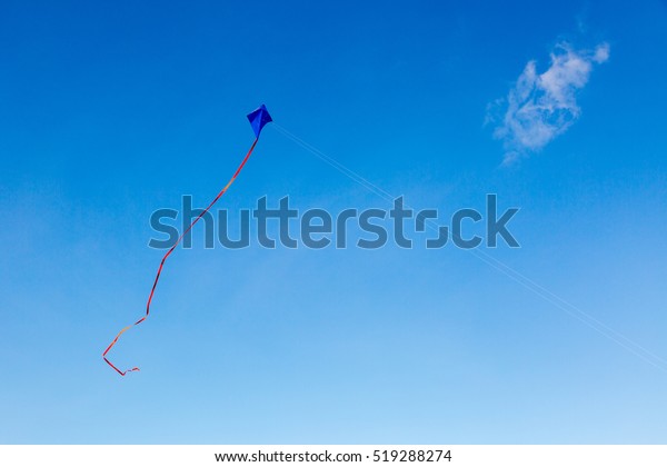 Blue kite with red tail on\
blue sky