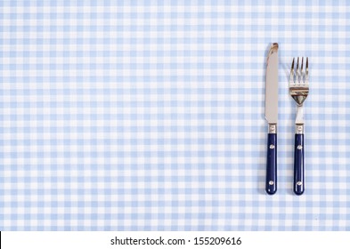 Blue Knife And Fork On A Checkered Table Cloth With Text Space