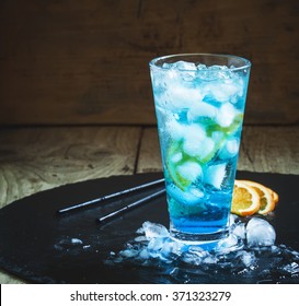 Blue Lagoon cocktail with orange and ice in a tall glass, dark toned image, selective focus
