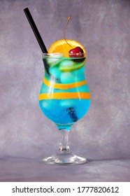 Blue lagoon cocktail, a tall glass with a drink, ripe cherries, a slice of orange and a straw on a gray background. Vertical positioning.