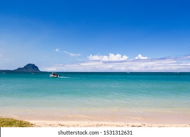 Blue lagoon and sandy beach with boat and mountain in background in Mauritius