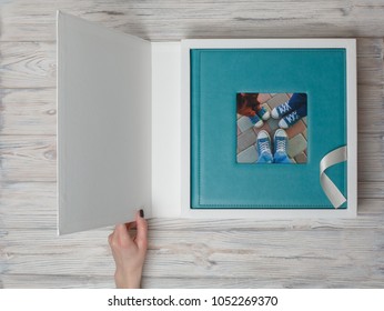 Blue Leather Photo Album In A Cardboard Box.
Family Photo Book With Leather Cover In Gift Box With Ribbon.
Womans Hand Open Box With Photo Album.
Person Is Looking At The Photo Book On The Table.