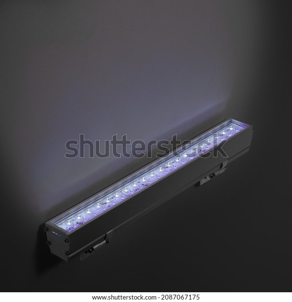 Blue LED flood light in aluminum housing with\
wire on dark background.