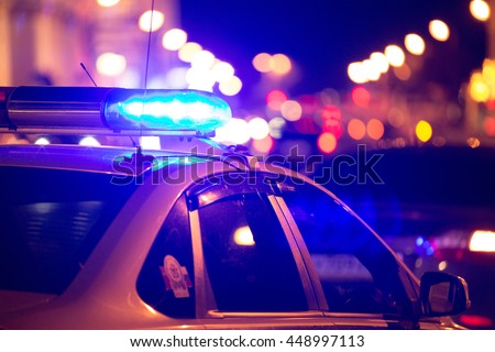 Blue light flasher atop of a police car. City lights on the background. 