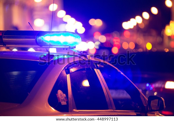 Blue light flasher atop of a police car. City lights on\
the background. 