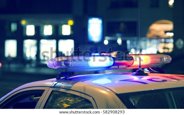 Blue light flasher atop of a police car. City\
lights on the background.