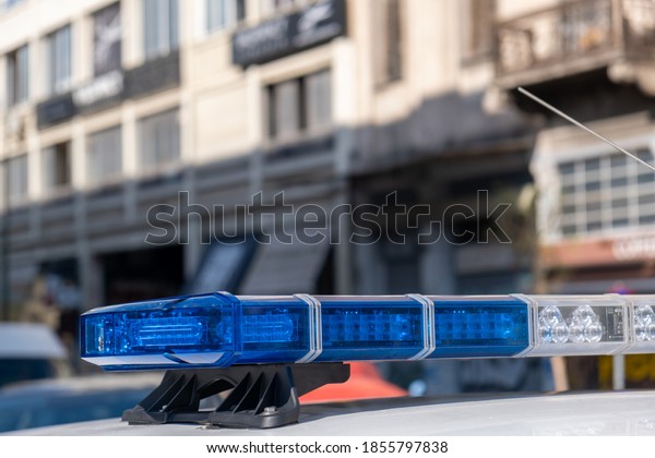 Blue light flasher at police car top\
closeup view, blur cityscape background. The roof mounted lightbar\
and siren, emergency vehicle, municipal\
police