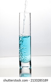 Blue Liquid Pouring Into Tall Glass On Bright Field High Key Background