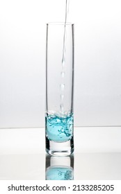 Blue Liquid Pouring Into Tall Glass On Bright Field High Key Background