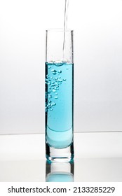 Blue Liquid Pouring Into Tall Glass On Bright Field High Key Background