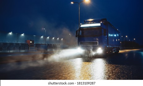 Blue Long Haul Semi-Truck with Cargo Trailer Full of Goods Travels At Night on the Freeway Road, Driving Across Continent Through Rain, Fog, Snow. Industrial Warehouses Area. - Shutterstock ID 1813109287