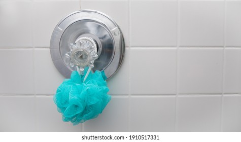 A blue loofah sponge hanging in a dry shower on the temperature guage.