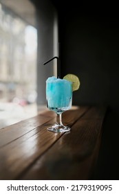 A Blue Margarita Cocktail With A Slice Of Lime Is On The Table. The Composition Of The Cocktail Includes Tequila, Blue Curacao Liqueur, Margarita Mix