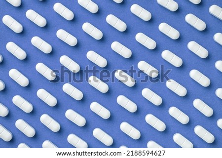 Blue medicine background with white pills and tablet, macro. Drug production backdrop. Medical pattern from vitamin capsule, closeup.