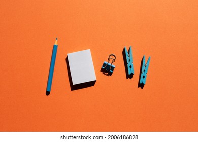 Blue memo notepad, clips, colored pencil on red background. Work and study place. flat lay, top view, copy space