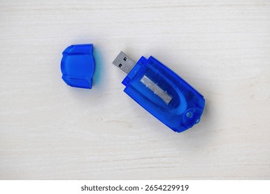 Blue memory card reader on light wood. Cap sits beside it. Top view, detailed close-up. Essential tech accessory for data transfer and digital storage. Perfect for electronics concepts.
