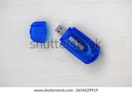 Blue memory card reader on light wood. Cap sits beside it. Top view, detailed close-up. Essential tech accessory for data transfer and digital storage. Perfect for electronics concepts.