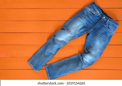 Blue mens jeans denim pants on orange background. Contrast saturated color. Fashion clothing concept. View from above