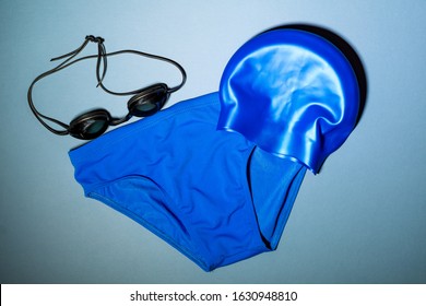 Blue Men's Swim Gear On A Blue Background. Swim Briefs, Swim Cap, And Swim Goggles.