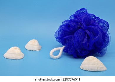 Blue mesh pouf bath sponge washcloth with sea shells on blue background closeup photo with copy space. Soft synthetic shower wash cloth. Washing hygiene design element. Spa body care accessory product