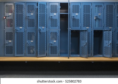 Blue metal cage lockers with a wood bench in a locker room with some doors open and some doors closed