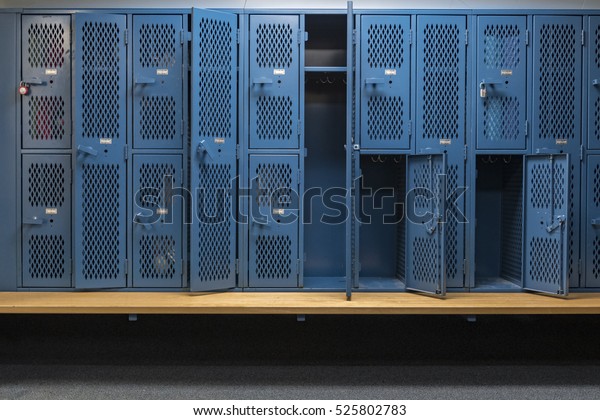 Blue metal cage lockers\
with a wood bench in a locker room with some doors open and some\
doors closed