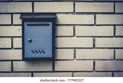 Blue metal mailbox mounted on the brick wall, mailbox has a letter engraving on it