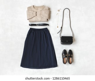 Blue midi pleated skirt, beige knitted sweater, small black cross body bag, belt, loafers (flat shoes) on grey background. Overhead view of women's casual day outfit. Flat lay, top view. Women clothes - Shutterstock ID 1286110465