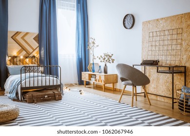 Blue, modern bedroom interior for a boy with gray armchair at a wooden desk and bed with metal frame