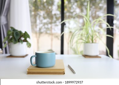 Blue modern matte coffee cup and pencil and brown notebook on white table with plants pot and keyboard - Powered by Shutterstock