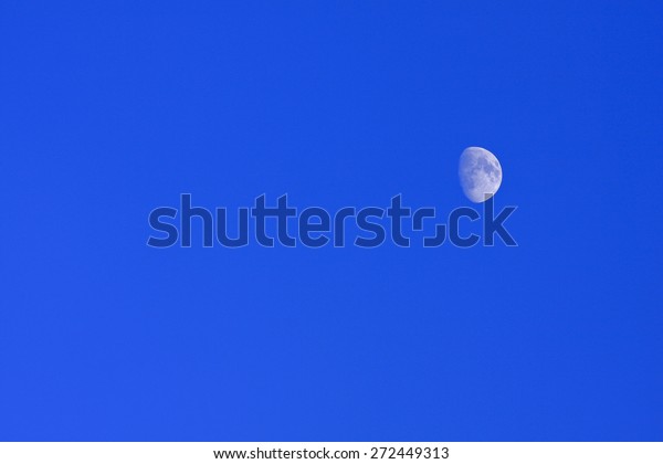 Blue moon of the Nordic bright sky. Half\
moon against a bright blue afternoon\
sky.