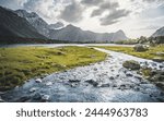 Blue mountain lake and river in a mountain valley among vegetation against the backdrop of rocky peaks with snow in the Fan Mountains in Tajikistan, Tien Shan highlands in the evening