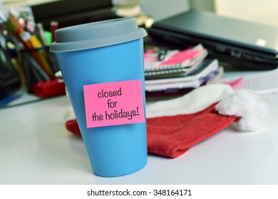 A Blue Mug With A Pink Sticky Note With The Text Text Closed For The Holidays On An Office Desk