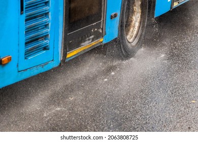 Blue Municipal Bus Moving On Rainy Road With Water Splashes - Close-up On Wheel