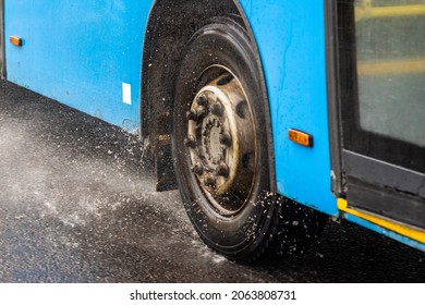 Blue Municipal Bus Moving On Rainy Road With Water Splashes - Close-up On Wheel