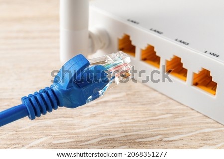 Blue network cable plug almost inserted into the yellow socket of white wi-fi wireless router. Wlan router for home and office for internet connection. Internet hardware concept. Close-up.