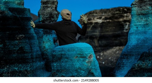 Blue Night And Alien Ufo Mask Between Rocks. Concept Of Aliens Among Us. Space Discover And Future With Extraterrestrial Life. Horror Creepy Concept Image With Monster And Scary Background