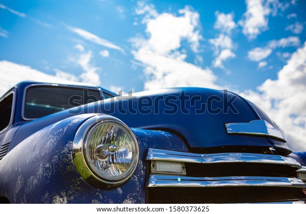 blue old classic antique American pickup\
car front part, low angle against the sky, close up on glass\
headlights lights lamps and the chrome\
grille