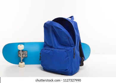 Blue Open Backpack Next To Skateboard On White Background, Back To School