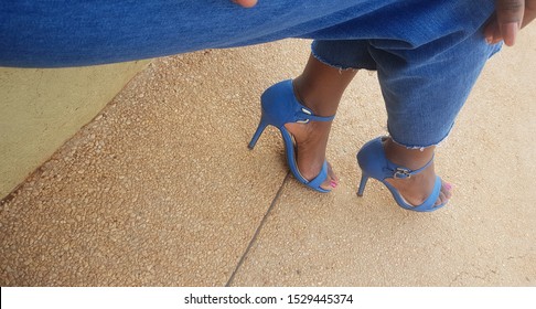 Blue Open Toe Stilleto Heels Worn By Woman In Baggy Blue Denim Cutoff Pants.  Shoe On Paved Surface