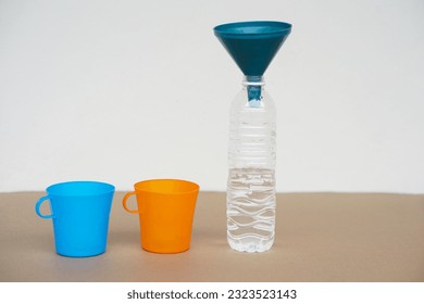 Blue and orange cups , bottle of water and funnel on the top. Concept, equipment for doing experiment, measuring liquid quantity.      